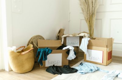 Three labeled cardboard boxes marked "Keep," "Donate," and "Trash" filled with clothing during a home decluttering process.